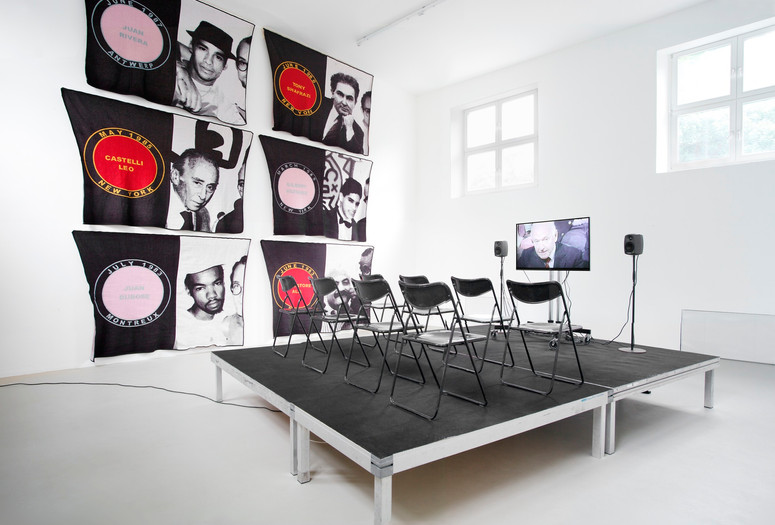 James Richards. Foreground: Active Negative programme. 2008. Video (color, sound). 20 min. Background: Untitled Merchandise (Lovers &amp; Dealers). 2012. Six machine-knitted nylon blankets. 152 x 228 cm. Installation view from The Imaginary Museum, Kunstverein Munich, 2012. Courtesy the artist and Rodeo, Istanbul and London and Cabinet, London