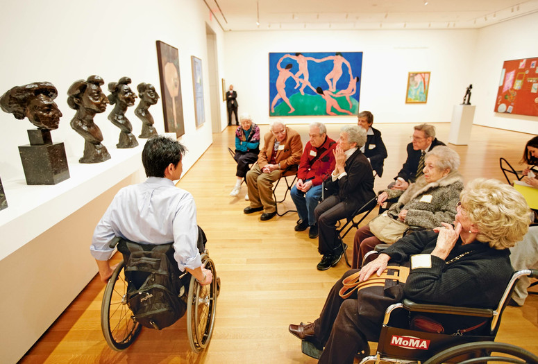 Photo: Jason Brownrigg ©️ 2023 The Museum of Modern Art, New York. Image description: An educator in conversation with a seated group of 10 adults facing a display of four sculpted bronze busts by the artist Henri Matisse in a gallery with colorful paintings on the wall.