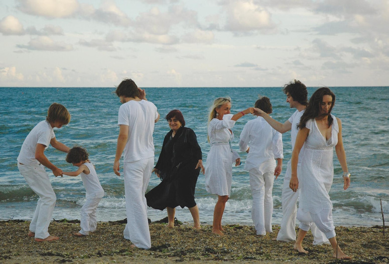 Les plages d’Agnès (The Beaches of Agnès). 2008. France. Written and directed by Agnès Varda. Courtesy of Cinema Guild/Photofest. ©️ Cinema Guild Image description: A group of seven individuals dressed in white are dancing on the beach. The central figure dressed in black, filmmaker Agnès Varda, smiles as she looks at the others engaging in movement and embracing one another.