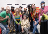 The Community Access Art Collective artists at their exhibition opening. Photo: Beatriz Meseuger/onwhitewall.com. ©️ 2024 The Museum of Modern Art, New York Image description: The Community Access Art Collective artists celebrate at their exhibition opening. Eleven colorfully dressed artists and studio staff pose in front of a backdrop with the MoMA logo printed in black and white. A person in the center holds a paper sign with the words "Thank You" written in blue ink, and two other people hold bouquets of flowers.
