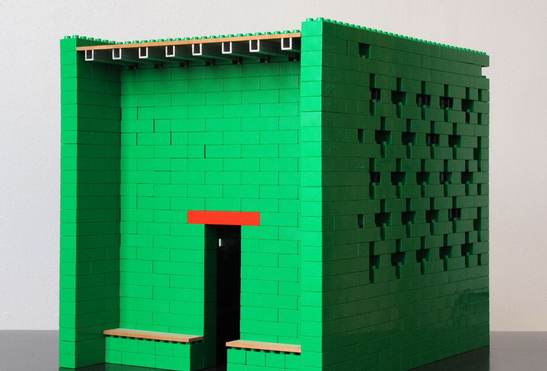 Thomas Schütte. Ackermans Tempel III (Modell 1:10) (Ackerman’s Temple III [Model 1:10]). 2011. LEGO bricks, wood, and aluminum. Collection of the artist, Düsseldorf. Photo: Luise Heuter. © 2024 Thomas Schütte/Artists Rights Society (ARS), New York/VG Bild-Kunst, Bonn Image description: A hollow cube sculpture made of green LEGO bricks resembling a temple building. A tall door opening topped with a wide red LEGO brick leads to the shadowed interior. Bricks on the right wall are stacked to create a square cross pattern. A thin piece of wood lines the rooftop, upheld by square aluminum brackets. Two wood-lined benches are built on either side of the door.