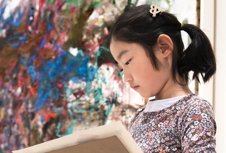 Photo: Martin SeckImage description: A child looks at her own artwork while standing in front of a painting.
