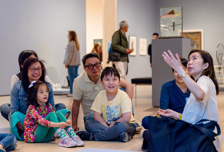 Photo: On White Wall, Inc.Image description: An instructor explains an artwork to smiling families.