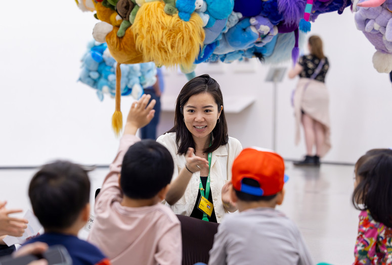Photo: On White Wall Inc.Image description: An educator engages a group of children in front of a hanging sculpture.