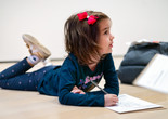 Photo: On White Wall Inc.Image description: A child lies on the Museum gallery floor while completing a worksheet.