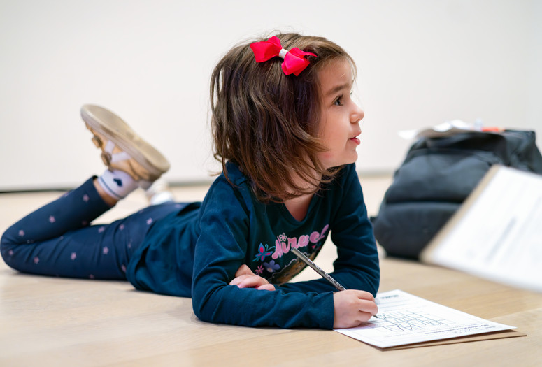 Photo: On White Wall Inc.Image description: A child lies on the Museum gallery floor while completing a worksheet.