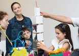 Photo: Martin SeckImage description: A child steadies a tower made out of cardboard while other workshop participants observe.