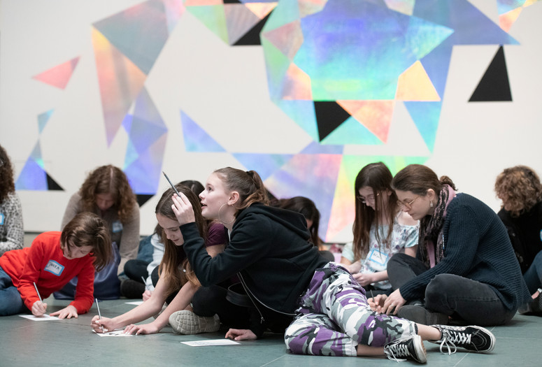 Photo: Martin SeckImage description: A tween points upwards with a pencil while other tweens draw on the gallery floor.