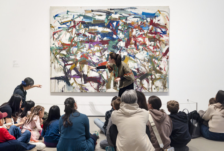 An educator points at streaks of paint in front of an artwork as families observe. Photo: On White Wall Inc.
