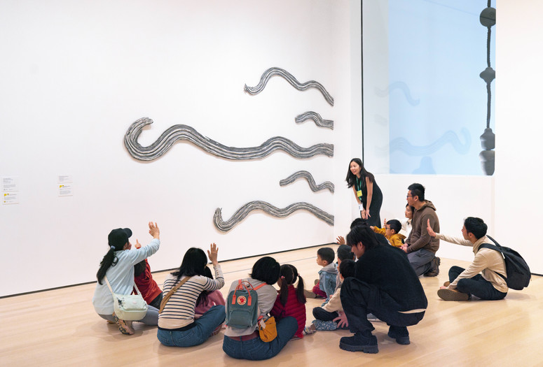 An educator leads a discussion with families in front of an artwork with large, cut-out, squiggly lines. Photo: On White Wall