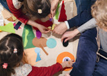 A group of four family members, photographed from above, add felt shapes of different colors to a background. Photo: On White Wall, Inc.