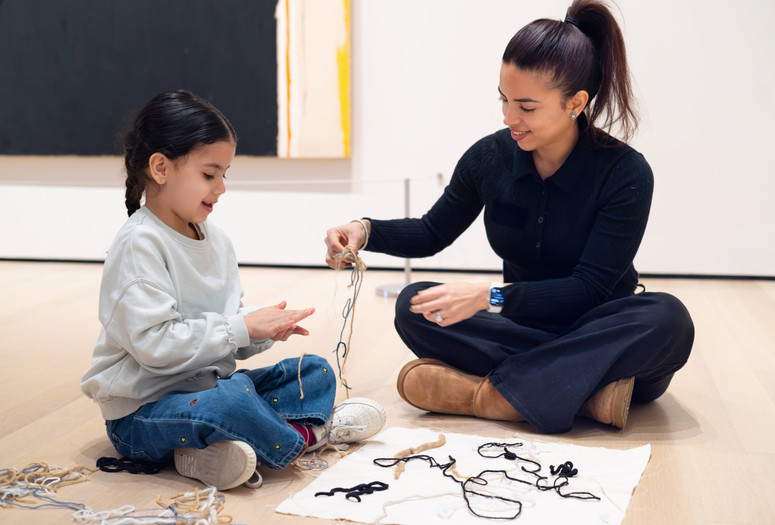 A child and an adult sit on the floor in the galleries arranging a composition with string. Photo: On White Wall, Inc.