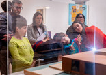 Families look at a work of art while a child and an educator tilt their heads to the left. The child holds his hands out in front of him. Photo: On White Wall, Inc.