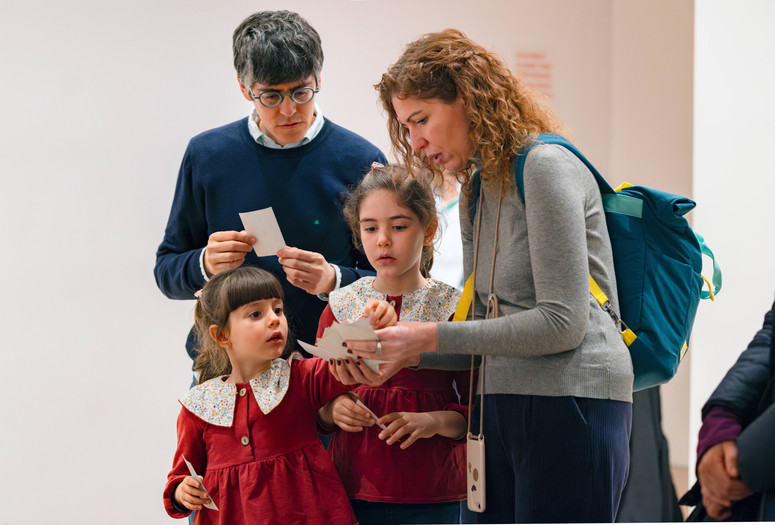 A group of people are looking intently at papers in their hands. The photo features predominant colors of red and blue. Photo: On White Wall, Inc.