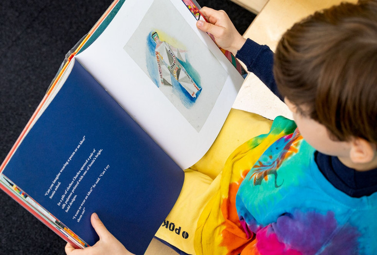 A child looks down at a picture book on his lap. Photo: On White Wall, Inc.