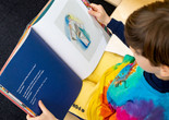 A child looks down at a picture book on his lap. Photo: On White Wall, Inc.