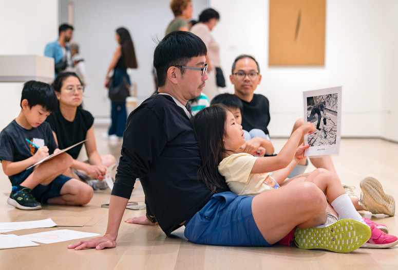 During a gallery talk, a child sits in their adult’s lap and points to an image of the artist Jackson Pollock splattering paint. Photo: On White Wall, Inc.