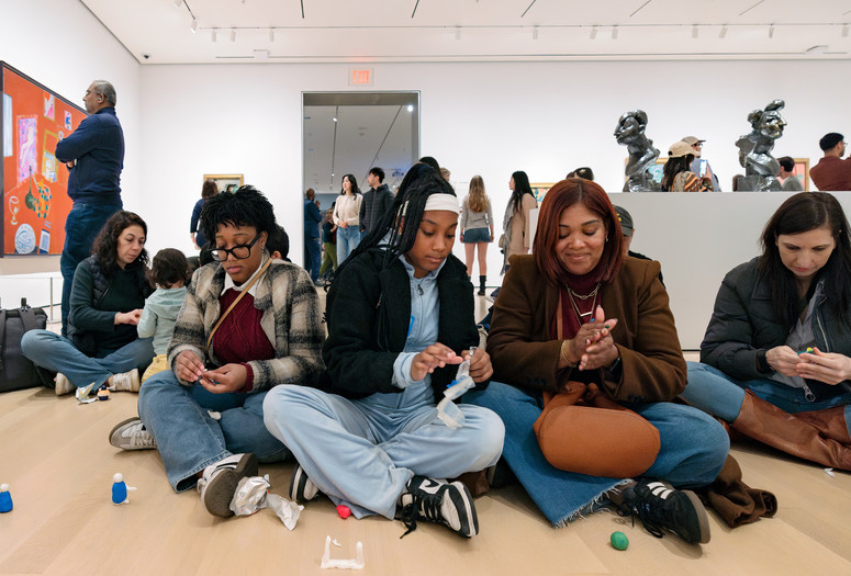 A parent and two teens sit on the floor of the galleries and make small sculptures using model magic. Photo: On White Wall, Inc.