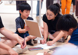 A parent and child sit on the gallery floor looking at each other and working on a drawing activity. Photo: On White Wall, Inc.