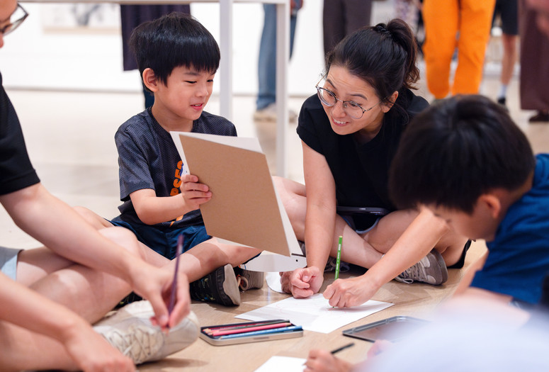 A parent and child sit on the gallery floor looking at each other and working on a drawing activity. Photo: On White Wall, Inc.