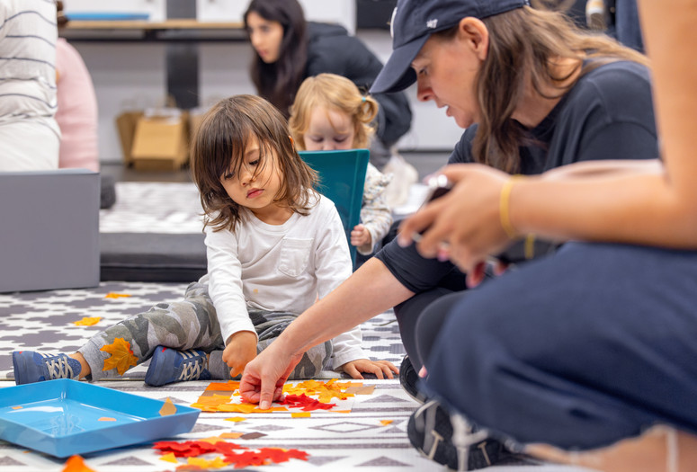 A caregiver and two children work together with orange tissue paper to make a collage. Courtesy: On White Wall, Inc.