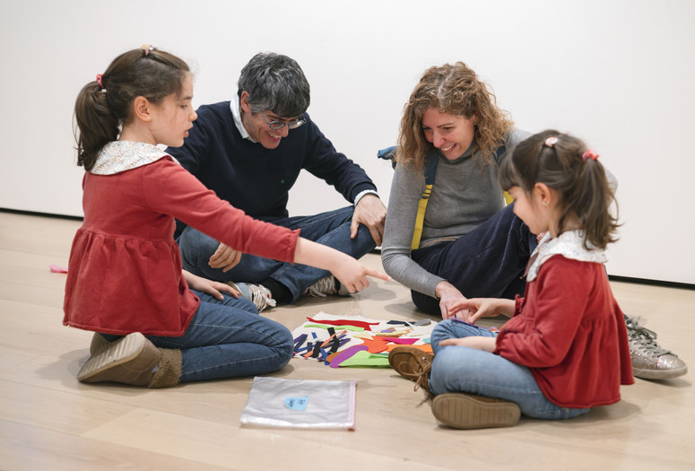 A family sits on the floor of the gallery and works on a collage with brightly colored felt shapes. Photo: On White Wall, Inc.