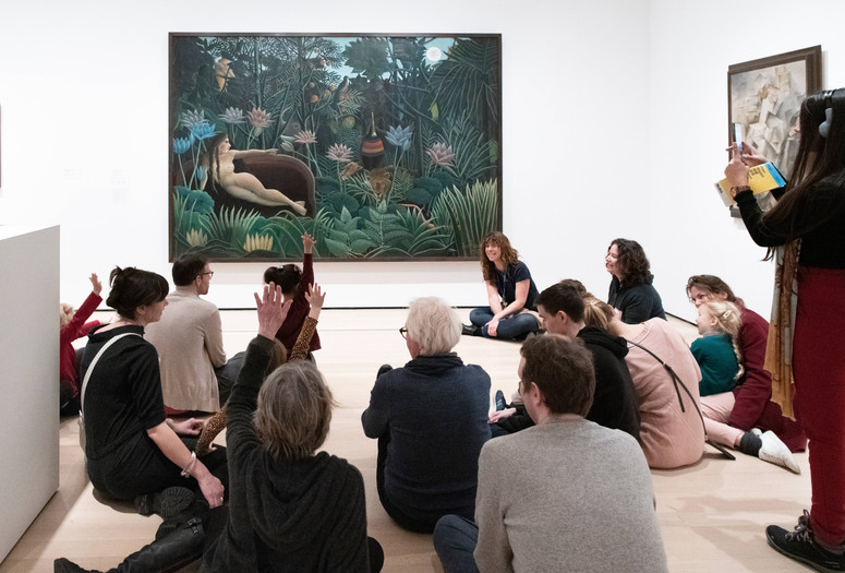An educator leads a discussion with families in front of a painting featuring a nude woman and a tiger in a jungle. Photo: Martin Seck