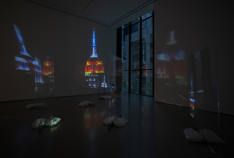 Lutz Bacher. Empire. 2014. High-definition video (color, sound, 10:43 min), two projectors, Plexiglas, sandbags, and metal stands. The Museum of Modern Art, New York. Acquired through the generosity of Lonti Ebers. © Lutz Bacher. Courtesy of the Estate of Lutz Bacher and Galerie Buchholz Image description: A room houses an artwork featuring projections of the Empire State Building at night on plexiglass.