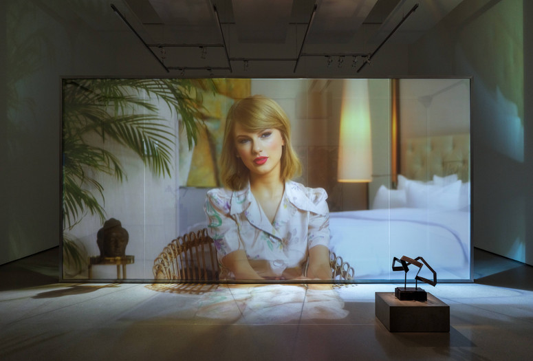 Christopher Kulendran Thomas. Being Human. 2019. High-definition video (color, sound; 24 min.) projected on glass, with three paintings and three sculptures: Untitled II, Untitled V, and Untitled VI (2018) by Upali Ananda, and Untitled II and Untitled V (2018) by Kingsley Gunatillake (all purchased by the artist from Saskia Fernando Gallery, Colombo); and Untitled X after Kingsley Gunatillake (2019) by Christopher Kulendran Thomas. In collaboration with Annika Kuhlmann. The Museum of Modern Art, New York. Acquired through the generosity of Charles Asprey and Markus Hannebauer. © 2026 Christopher Kulendran Thomas