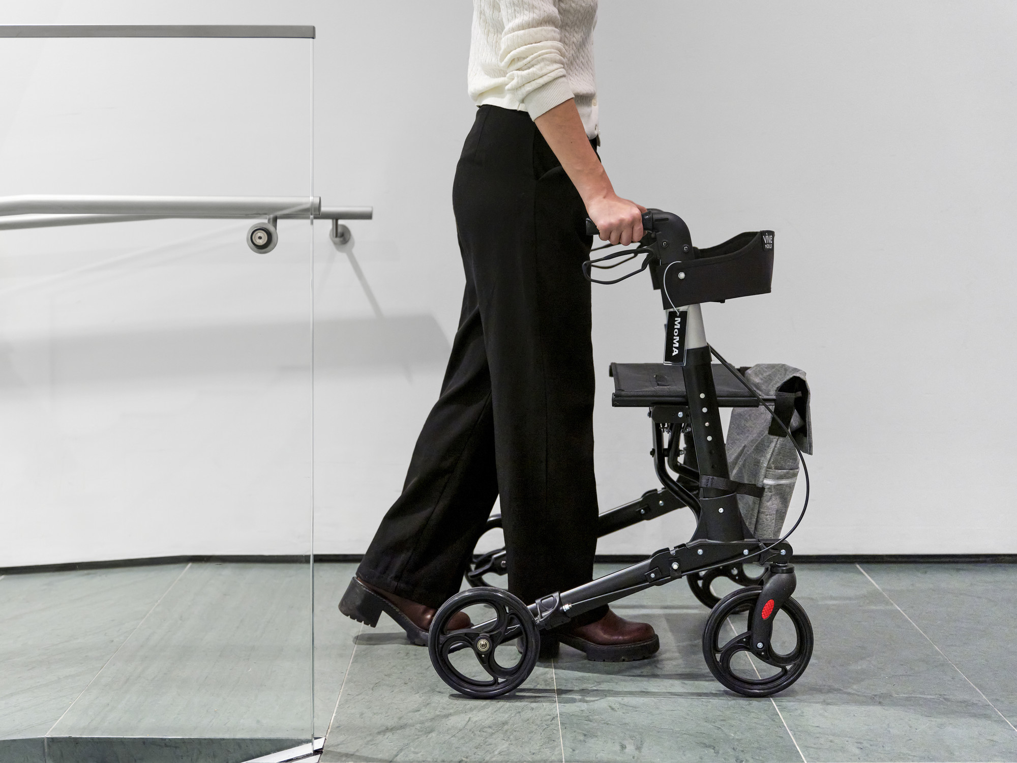Photo: Matthew ShermanImage description: A black by-request MoMA rollator being pushed up a ramp by a person in black pants.