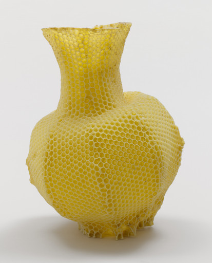 A bright yellow vase with a honeycomb texture and a narrow, flared top stands against a plain white background. The vase bulges in the middle and tapers at the bottom. This is an AI generated description. To give feedback, email ai@moma.org.