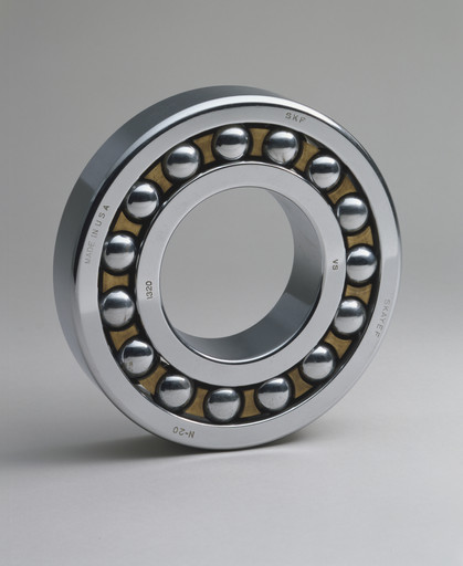 A metallic circular ball bearing with visible steel balls is shown against a plain gray background. The bearing has a silver outer ring with text, and a gold inner frame holding the balls. This is an AI generated description. To give feedback, email ai@moma.org.
