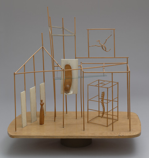 A wooden and wire sculpture features geometric shapes and abstract forms in brown and beige. It stands on an oval base with a neutral gray background. This is an AI generated description. To give feedback, email ai@moma.org.