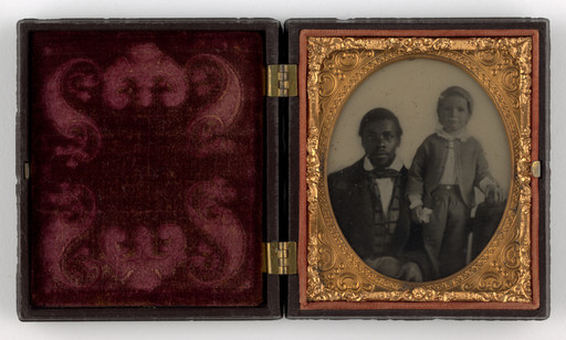 An old photograph in a gold frame within a hinged case shows a seated person in formal attire and a standing child. The left side of the open case is lined with dark red velvet featuring ornate patterns. This is an AI generated description. To give feedback, email ai@moma.org.